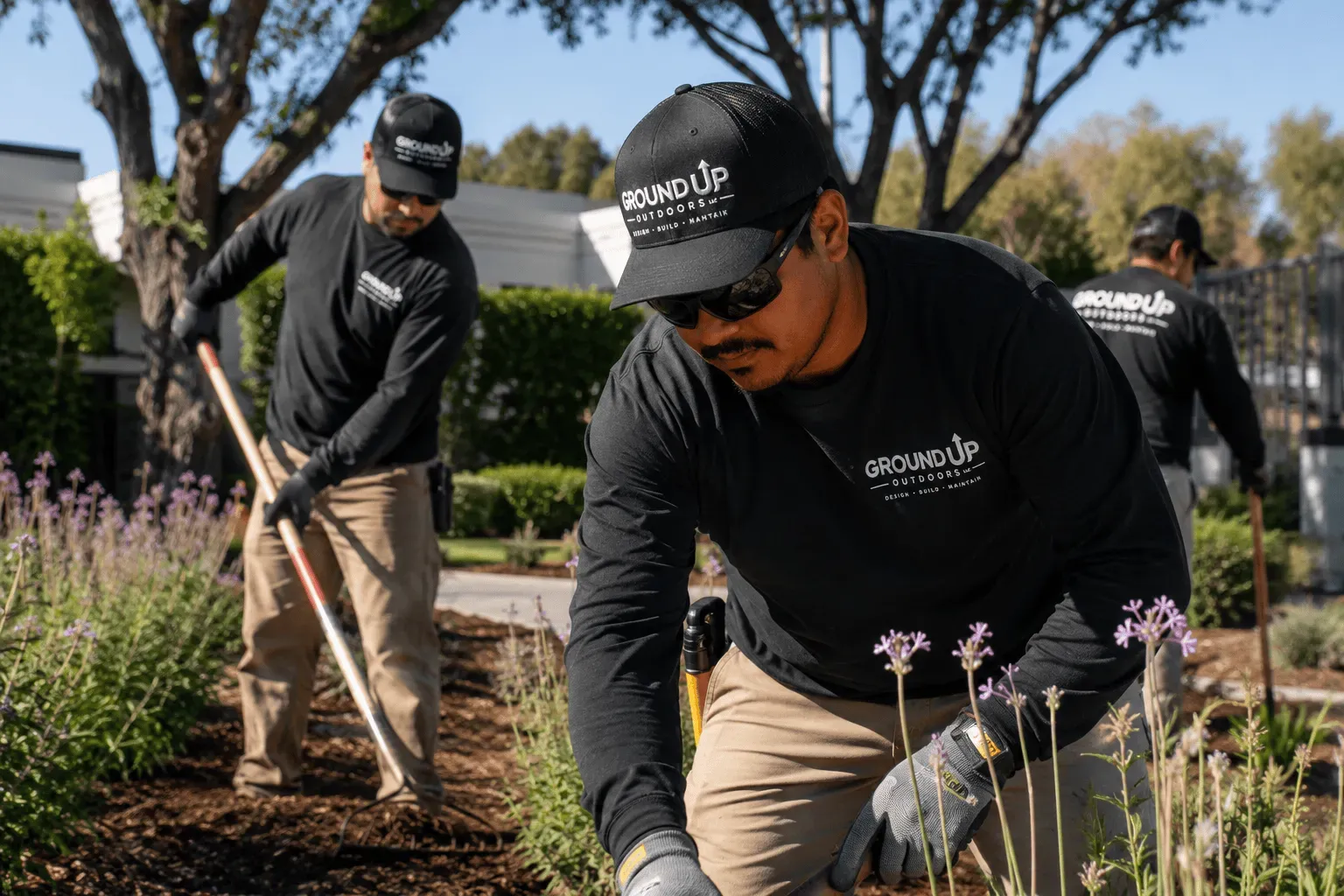 Ground Up Outdoors crew in branded uniforms hand-working a Southern California garden bed